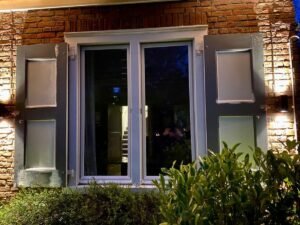 Elegante up-and-down LED wandlampen gemonteerd naast klassieke luiken van een woonhuis.