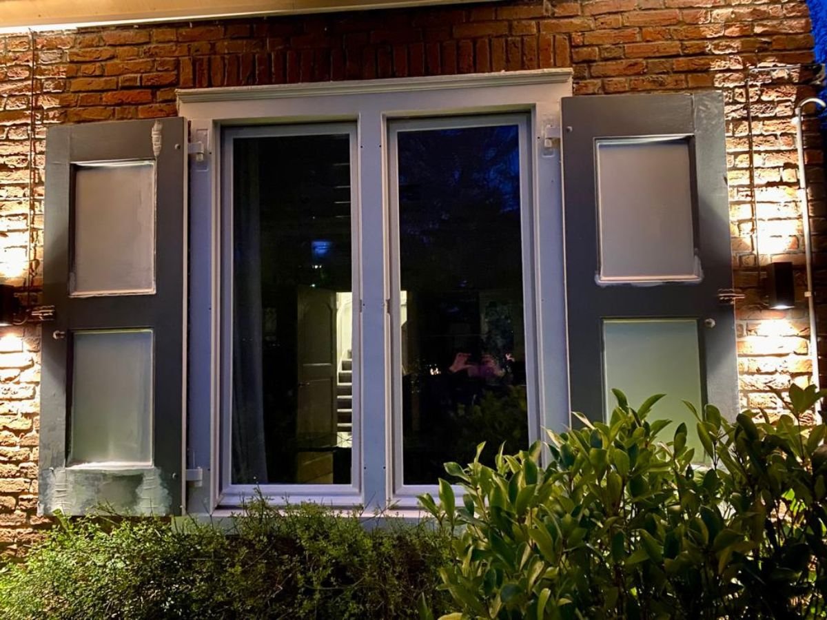 Elegante up-and-down LED wandlampen gemonteerd naast klassieke luiken van een woonhuis.