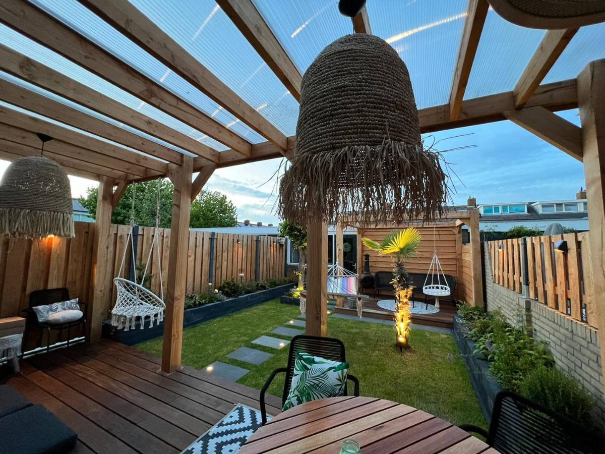 Luxe houten overkapping met sfeervolle buitenverlichting en een verlichte palmboom in de achtertuin.
