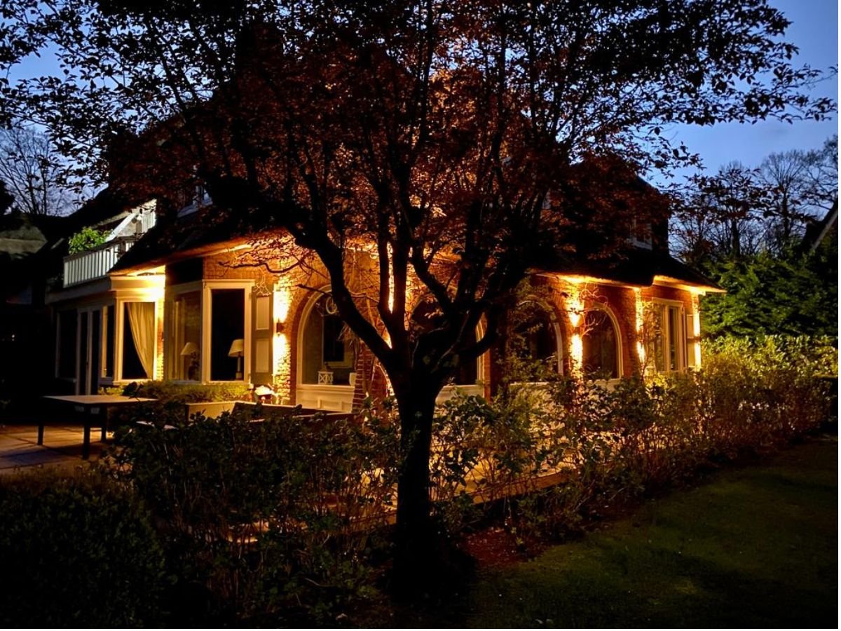 Complete architectonische buitenverlichting van een luxe villa met rieten dak en verlichte bomen in de tuin.