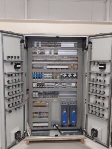 Binnenzijde van een industriële besturingskast met PLC-systemen en omvormers.