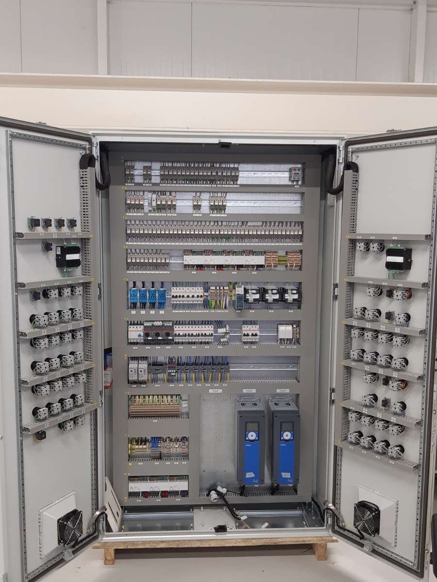Binnenzijde van een industriële besturingskast met PLC-systemen en omvormers.