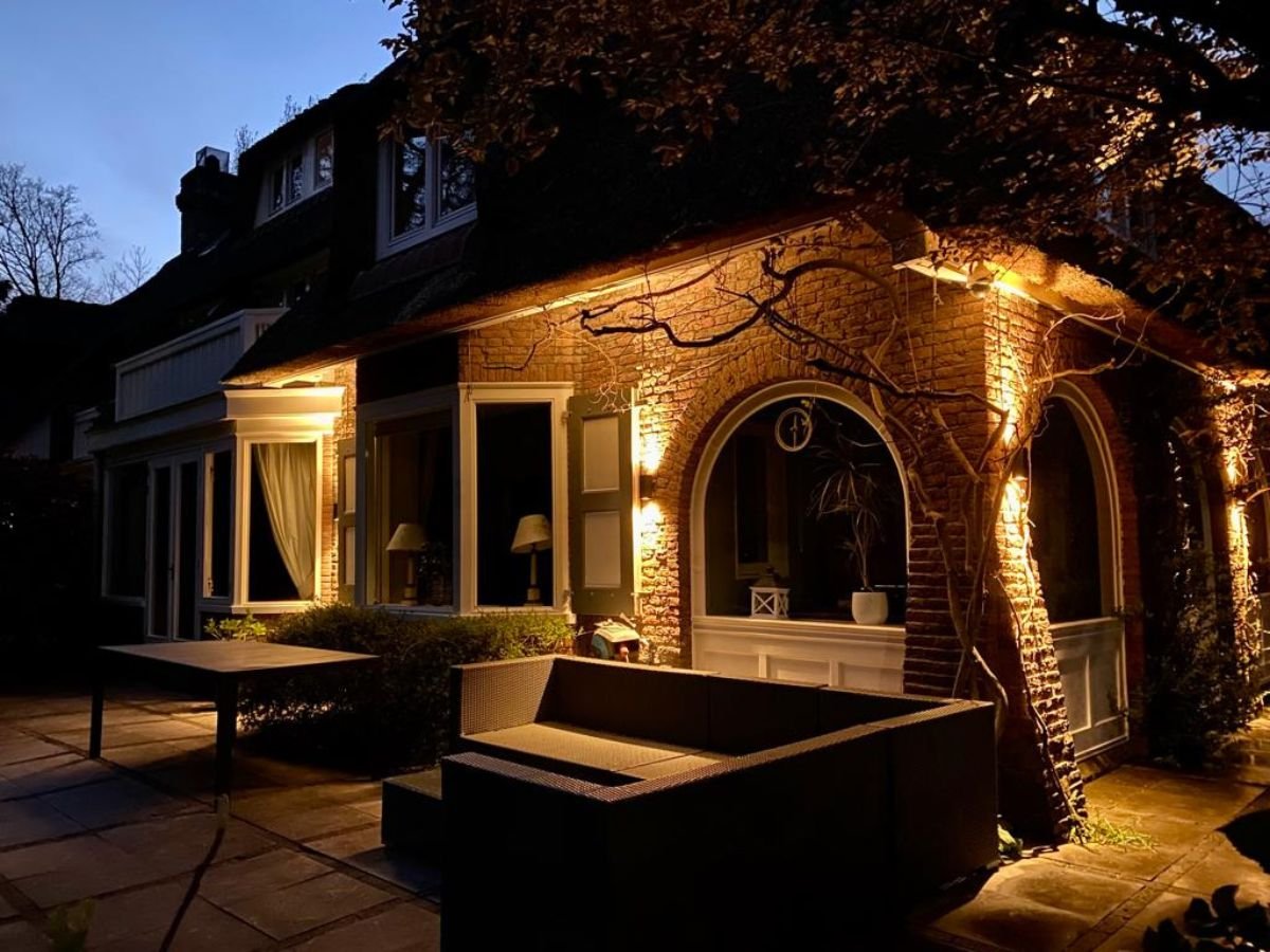 Sfeerverlichting rondom het terras en de gevel van een exclusief landhuis met boogramen.