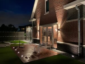 Warm witte LED wandlampen op een bakstenen gevel gecombineerd met geïntegreerde terrasverlichting.