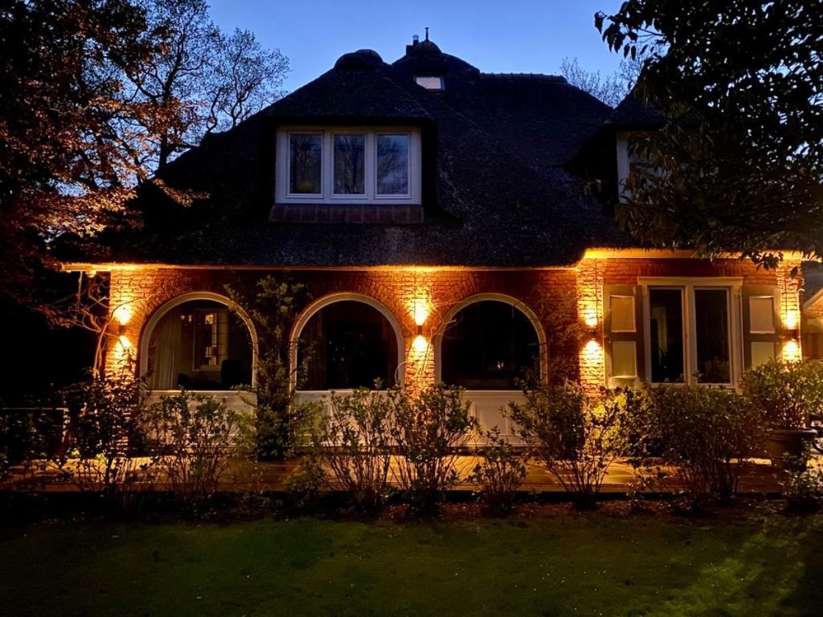 Warm witte LED buitenverlichting perfect uitgelijnd op de bakstenen gevel van een woning met rieten kap.