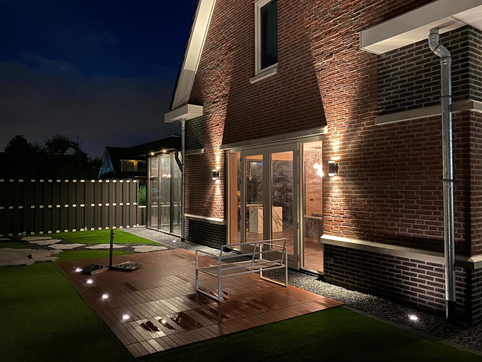 Warm witte LED wandlampen op een bakstenen gevel gecombineerd met geïntegreerde terrasverlichting.