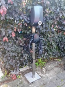 Elektrische auto oplader gemonteerd op een design paal in de tuin.