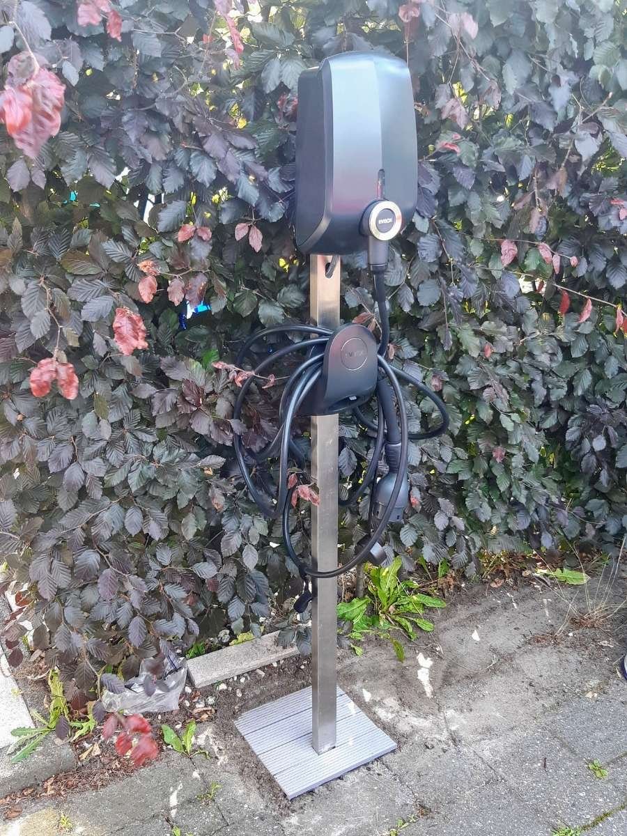 Elektrische auto oplader gemonteerd op een design paal in de tuin.